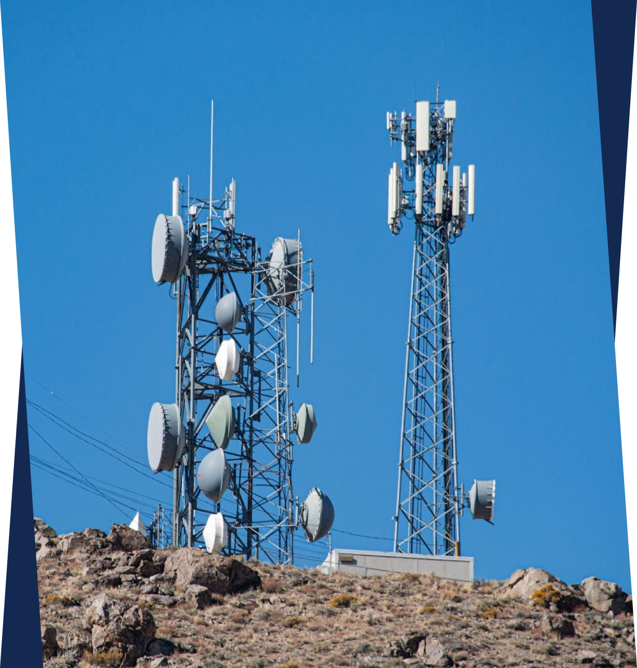 h1 3 Two tall communication towers on a rocky hilltop are equipped with various antennas and dishes against a clear blue sky.